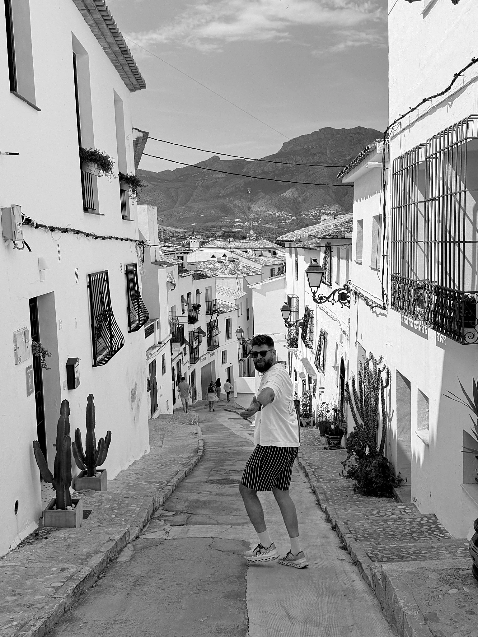 Mikhail Shal on a whitewashed Mediterranean village street with mountains behind him